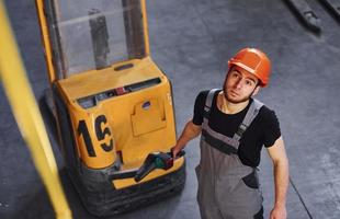 giovane maschio lavoratore nel uniforme è nel il magazzino spingendo pallet camion foto