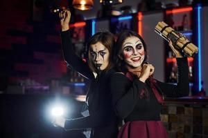 Due femmina amici è su il tematico Halloween festa nel pauroso trucco e costumi con tempo bomba foto