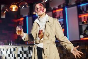 con bevanda nel mano. ritratto di uomo quello è su il tematico Halloween festa nel zombie trucco e costume foto