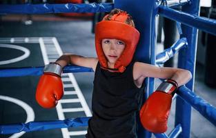 stanco ragazzo nel protettivo attrezzatura pendente su il nodi di boxe squillare foto