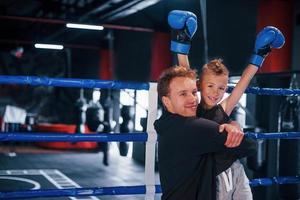 boxe allenatore in piedi nel il squillare con ragazzo e festeggiare vittoria insieme foto