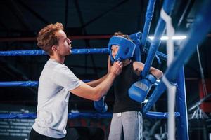 giovane boxe allenatore è porzione poco ragazzo nel protettivo indossare su il squillare fra il turni foto