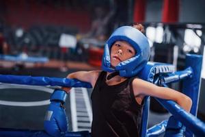 stanco ragazzo nel protettivo attrezzatura pendente su il nodi di boxe squillare foto