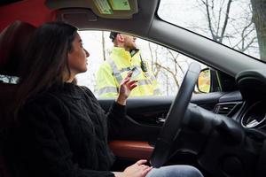 maschio polizia ufficiale nel verde uniforme controllo veicolo su il strada. donna provando per dare corrompere foto