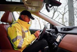 maschio polizia ufficiale nel verde uniforme seduta nel automobile e Lavorando con documenti foto