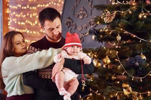 padre e madre con loro bambino decorazione albero insieme nel camera foto