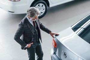 aereo Visualizza di alla moda vecchio uomo con grigio capelli e baffi quello guardare per un' nuovo auto in casa nel salone foto