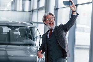 positivo anziano uomo con grigio capelli assunzione autoscatto contro moderno auto in casa foto