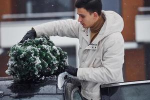 uomo nel bianca indossare mettendo Natale abete albero su il superiore di il suo auto all'aperto foto