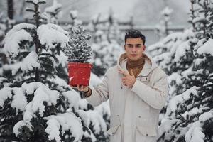 bello giovane uomo nel caldo cappotto Tenere rosso pentola con abete albero all'aperto a giorno foto