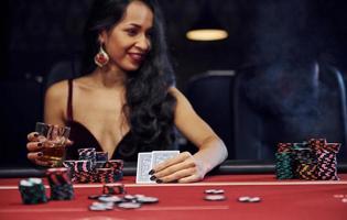 donna nel elegante Abiti si siede nel cassino di tavolo e giochi poker gioco foto