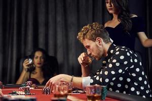 con bicchieri di bere. gruppo di elegante giovane persone quello giocando poker nel casinò insieme foto