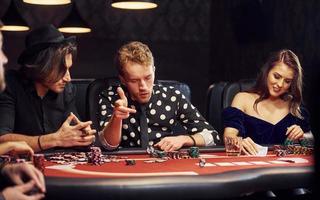 con bicchieri di bere. gruppo di elegante giovane persone quello giocando poker nel casinò insieme foto