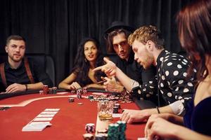 con bicchieri di bere. gruppo di elegante giovane persone quello giocando poker nel casinò insieme foto