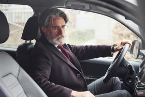 alla moda anziano uomo nel elegante Abiti è nel il moderno auto foto