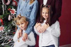 Due poco ragazze sta insieme con mamma e papà nel camera con Natale albero foto