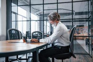 maturo uomo d'affari con grigio capelli e barba nel formale Abiti è nel il ufficio foto