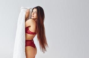 donna nel rosso biancheria intima copertura sua corpo di asciugamano nel il studio contro bianca sfondo foto