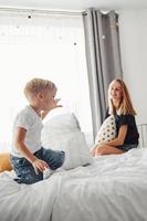 madre giocando cuscino combattimento con sua figlio nel Camera da letto a giorno foto