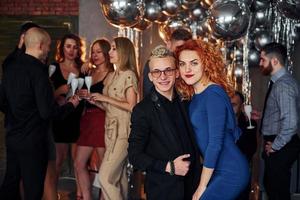 giovane uomo con testa Rossa donna è insieme contro loro amici nel Natale decorato camera e festeggiare nuovo anno foto