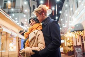 vicinanza di il le persone. contento giovane coppia nel caldo Abiti è su Natale decorato strada insieme foto