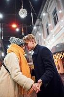 vicinanza di il le persone. contento giovane coppia nel caldo Abiti è su Natale decorato strada insieme foto