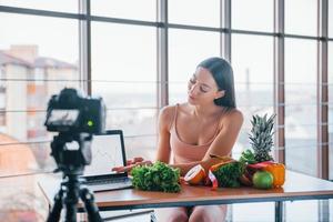 giovane fitness vlogger fare video in casa di seduta vicino tavolo con salutare cibo foto