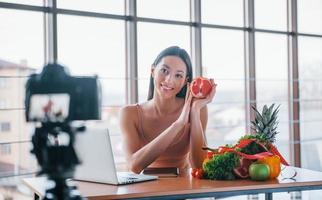 giovane fitness vlogger fare video in casa di seduta vicino tavolo con salutare cibo foto