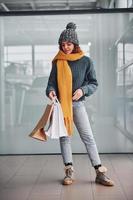 bellissimo allegro ragazza nel giallo sciarpa e nel caldo Abiti in piedi in casa con shopping borse nel mani foto