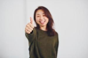 ritratto di contento asiatico giovane ragazza quello Spettacoli pollice su in casa nel il studio contro bianca sfondo foto