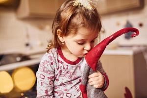 carino poco ragazza seduta e baci sua giocattolo su il cucina con cibo foto