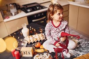 carino poco ragazza seduta e avere divertimento su il cucina con cibo foto