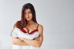 donna nel rosso biancheria intima copertura sua corpo di asciugamano nel il studio contro bianca sfondo foto