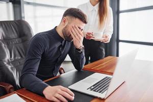 tipo si sente cattivo. donna e uomo nel formale Abiti Lavorando insieme in casa nel il ufficio di tavolo foto