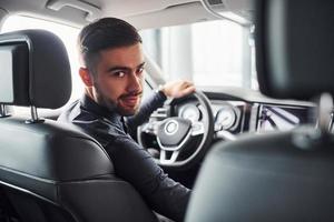 uomo nel elegante Abiti seduta nel marca nuovo costoso automobile foto