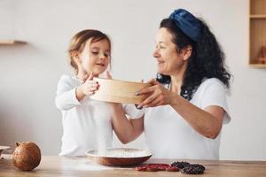 anziano donna con sua nipotina preparazione cibo con Farina su cucina foto