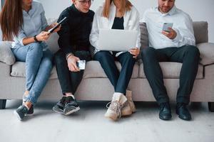 gruppo di amici seduta su il divano con il computer portatile e telefoni insieme foto