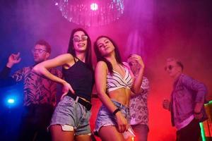 Due bellissimo ragazze danza nel davanti di giovane persone quello avendo divertimento nel notte club con colorato laser luci foto