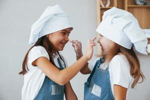 Due poco ragazze nel blu capocuoco uniforme avere divertimento con Farina su il cucina foto