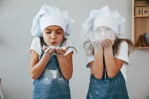 Due poco ragazze nel blu capocuoco uniforme colpi il Farina su di mani su il cucina foto