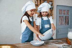 Due poco ragazze nel blu capocuoco uniforme Lavorando con Farina su il cucina foto