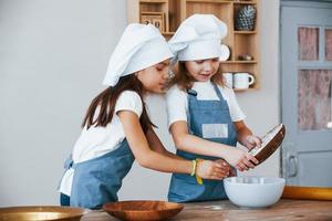 Due poco ragazze nel blu capocuoco uniforme Lavorando con Farina su il cucina foto