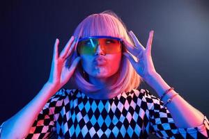 ritratto di giovane ragazza con biondo capelli nel occhiali nel rosso e blu neon nel studio foto
