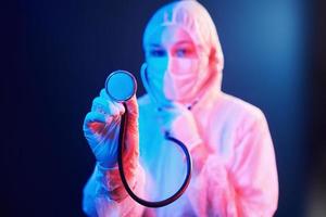 infermiera nel maschera e bianca uniforme e con stetoscopio in piedi nel neon illuminato camera foto