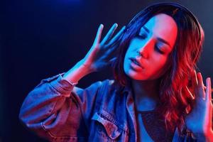 ritratto di giovane ragazza quello ascoltando per musica nel cuffie nel rosso e blu neon nel studio
