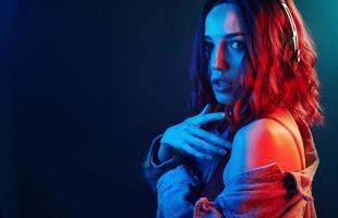 ritratto di giovane ragazza quello ascoltando per musica nel cuffie nel rosso e blu neon nel studio foto