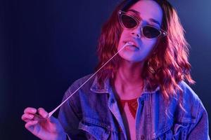 ritratto di giovane ragazza nel bicchieri con bolla gomma nel rosso e blu neon nel studio foto