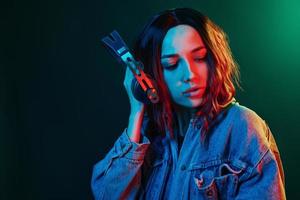 ritratto di giovane ragazza quello ascoltando per musica nel cuffie nel rosso e blu neon nel studio foto