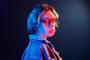 ritratto di giovane alternativa ragazza nel bicchieri con verde capelli nel rosso e blu neon leggero nel studio foto