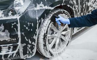 maschio lavoratore nel uniforme lavaggio nuovo moderno auto quello coperto con sapone. concezione di servizio foto